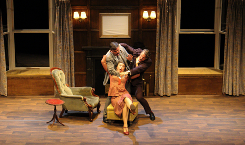 3 actors on stage in a farcical scene where one person is being strangled by another while the third is attempting to stop them